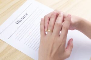 A woman pulling her wedding ring off her finger against background of divorce certificate.