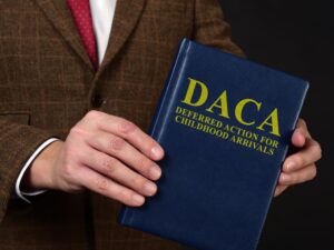 Deferred Action for Childhood Arrivals DACA concept. Man in suit shows the book.